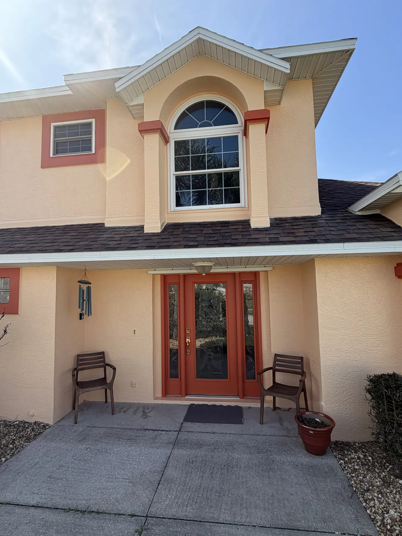 Freshly painted front entry with peach stucco walls, coral trim, and a deep red-orange double door