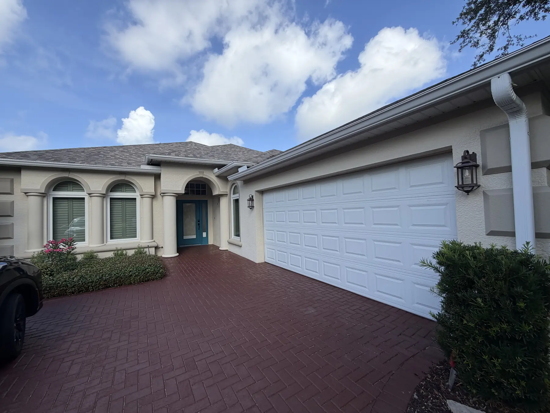 Full front elevation of a repainted stucco home with a white garage door and brick paver driveway