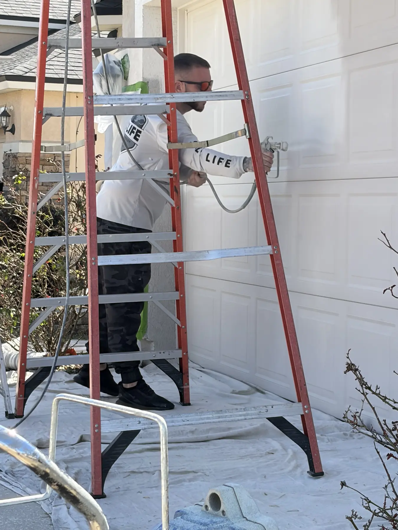 Painter spraying a fresh white finish coat onto a garage door