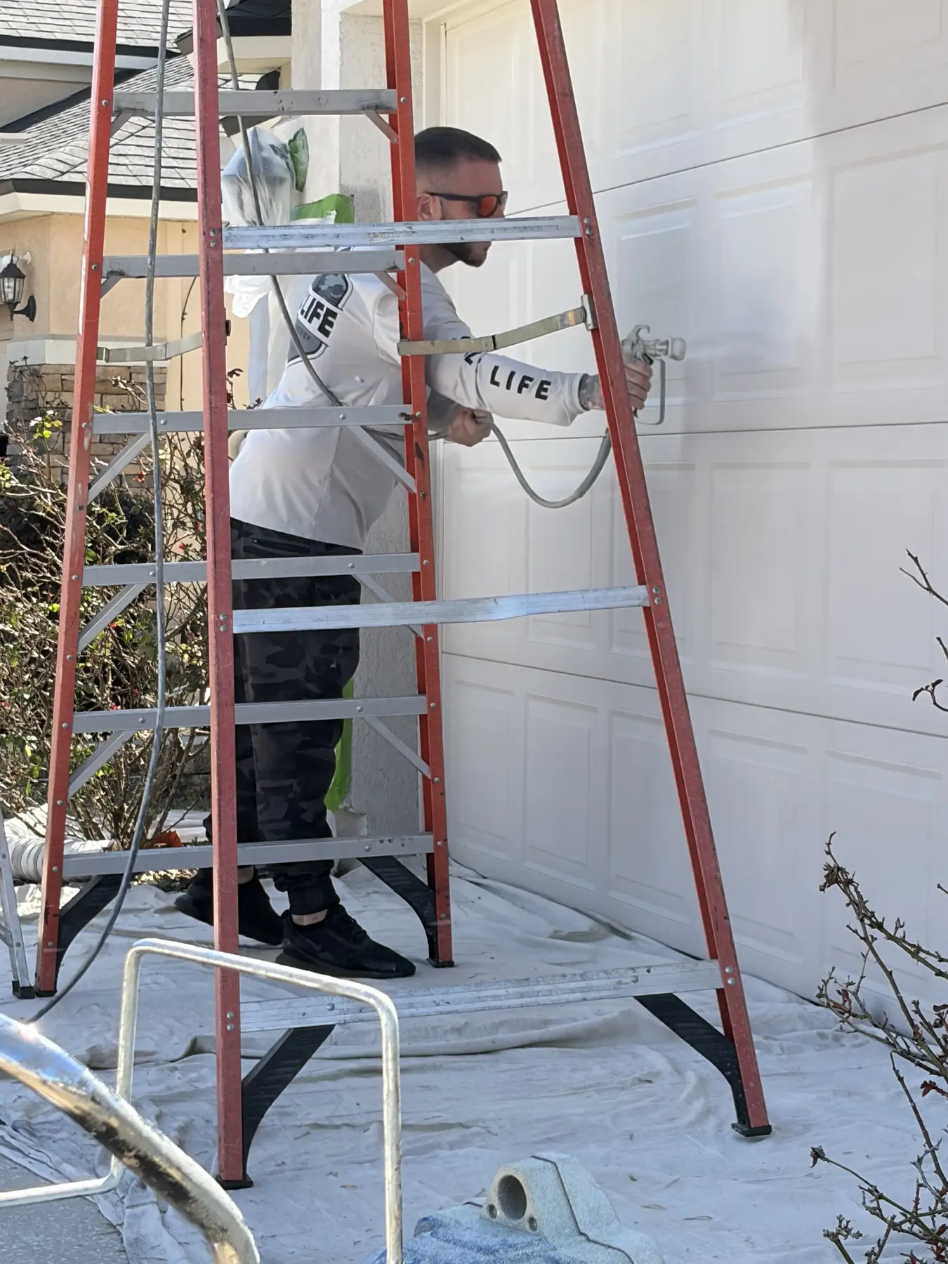 Technician applying a soft-wash treatment beside a residential garage