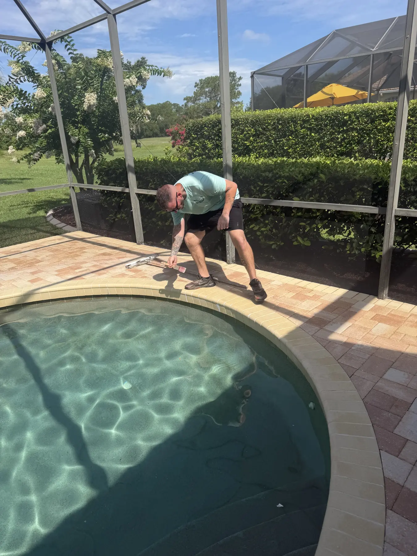 Technician cleaning pavers along the edge of a residential pool