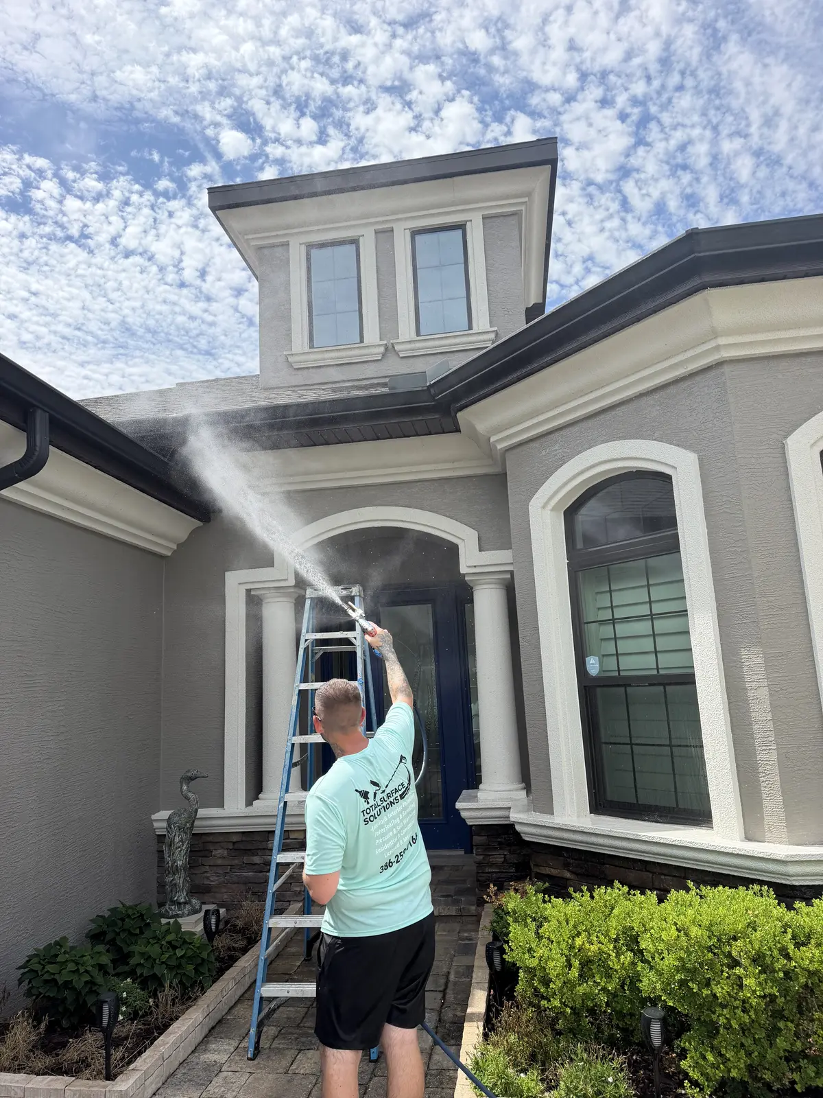 Technician soft washing the front of a two-story home