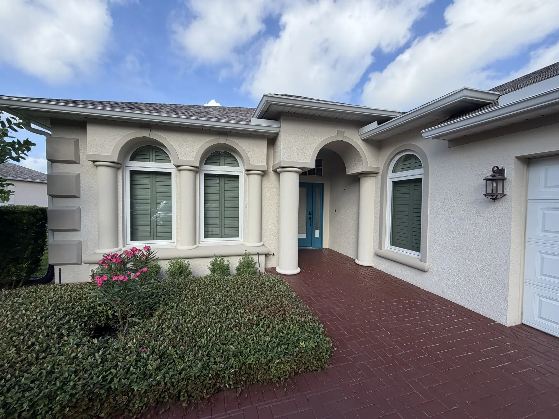 Front of a stucco home repainted in a soft cream with painted columns, arched window surrounds, and a teal front door