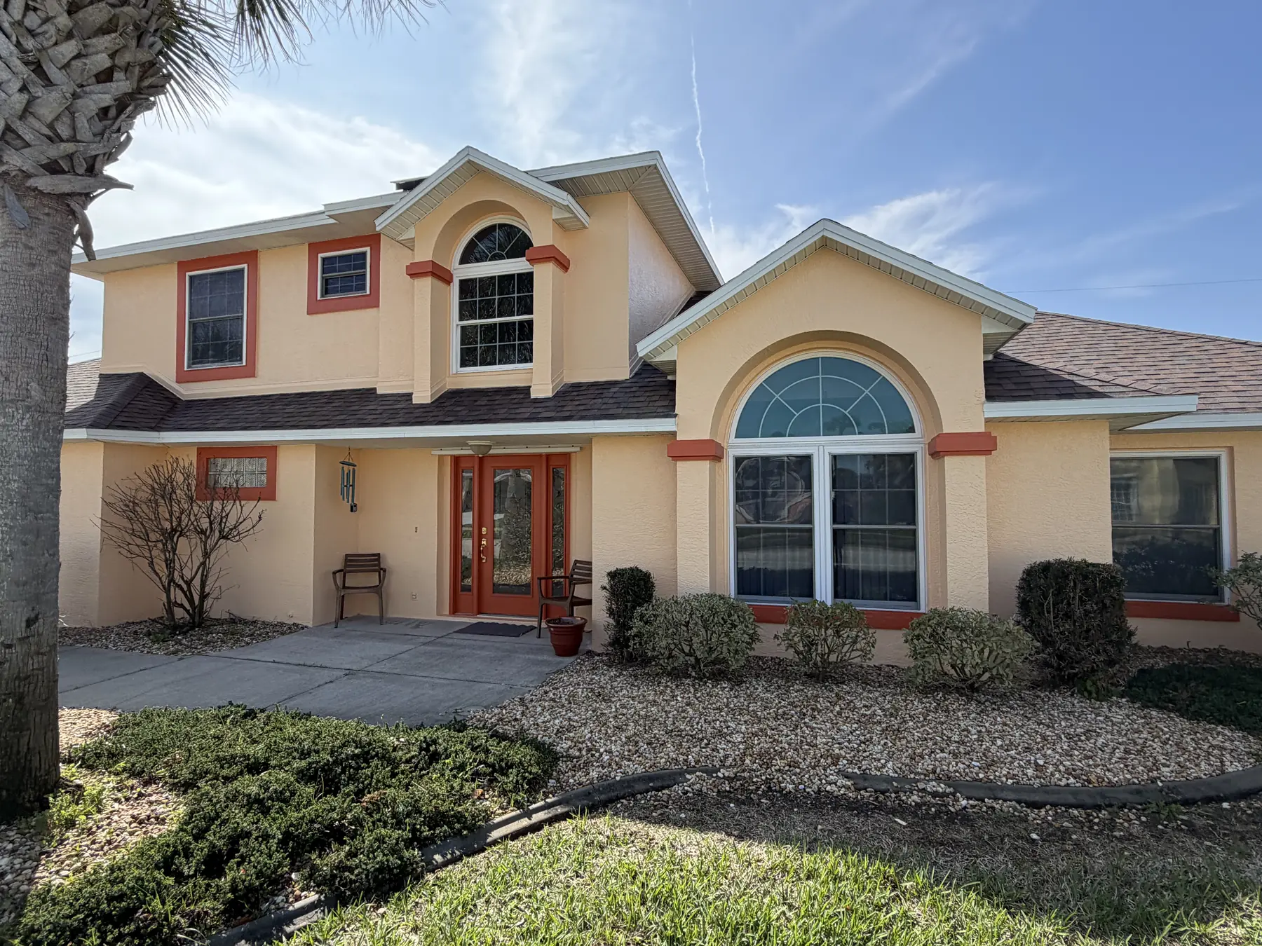 Two-story stucco home repainted in a warm peach body color with coral accent trim