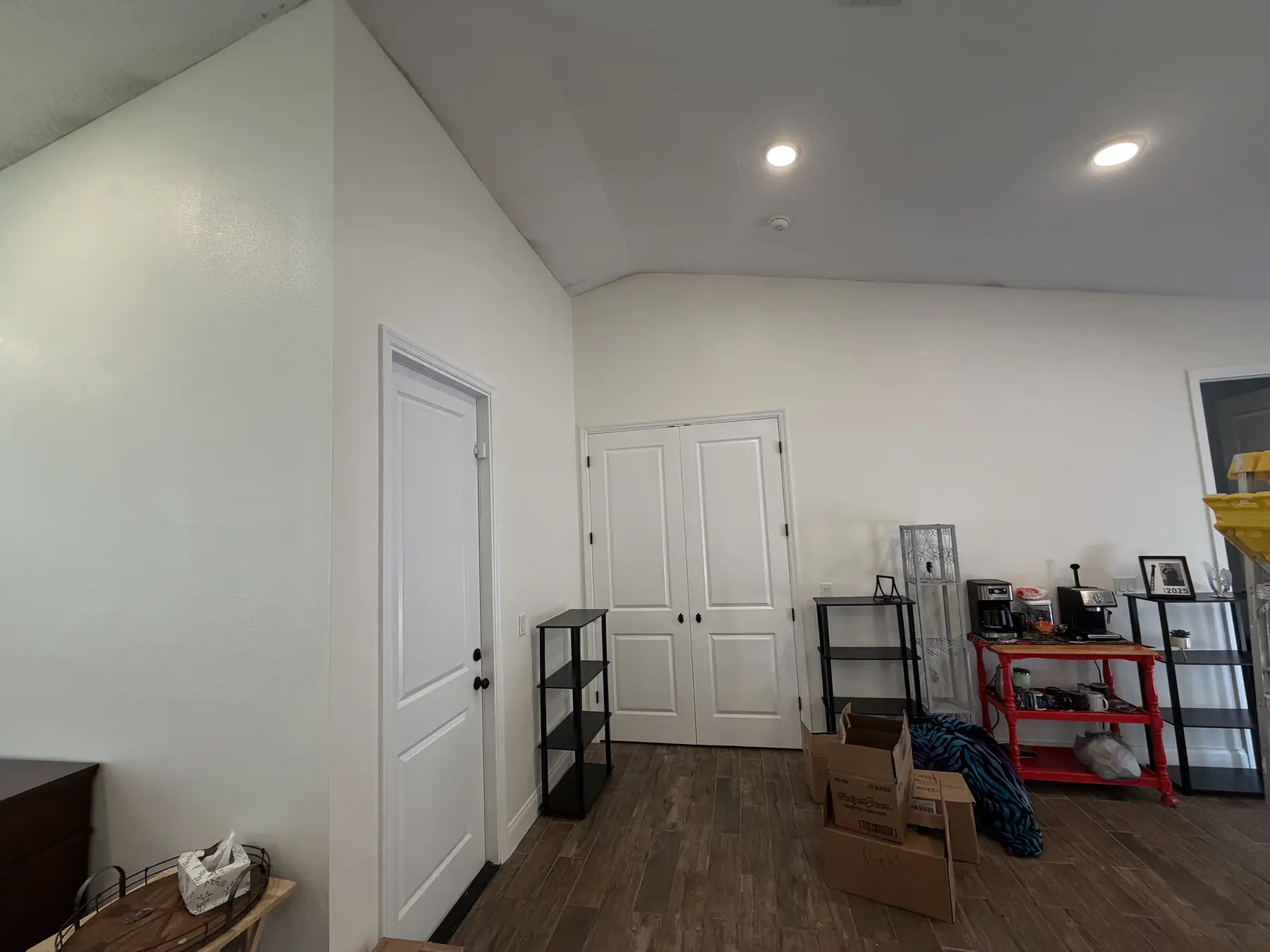 Room with a vaulted ceiling painted white along with the walls and double closet doors